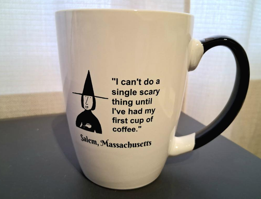 "I can't do a single scary thing until I've had my first cup of coffee." White, ceramic, 12 oz coffee mug with black handle and interior.